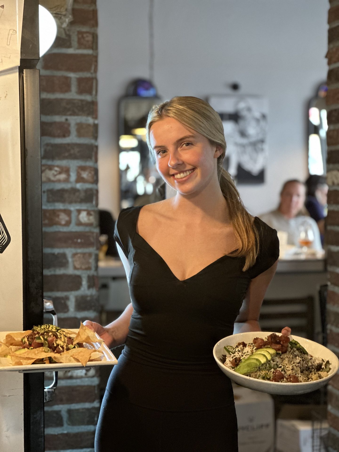 Server at Notorious Sports Bar & Grill in Carlsbad holding poke nachos and a fresh poke bowl